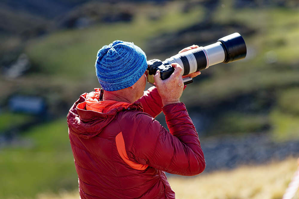 Middle aged male photographer taking pictures with telephoto lens at Air Display Axalp 2022 in the Swiss Alps on a sunny autumn day. Photo taken October 18th, 2022, Axalp, Switzerland.