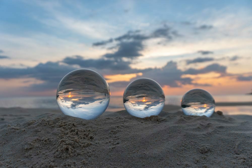 Three clear crystal balls of three sizes are sphere reveals seascape view with spherical placed on the sand at Karon Beach during sunset.